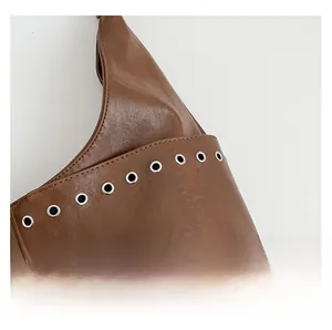 Detail of brown glossy leather tote featuring precision stitching and silver metal eyelets