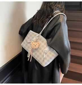 Detail of checkered tote bag with plush bear charm worn on a stylish indoor staircase