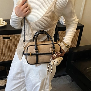Detail of beige and black contrast handbag with plush bear charm and pebbled leather texture