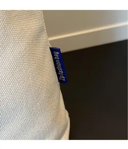Detail of blue woven logo tag on off-white canvas tote bag showing tight stitching
