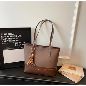Dettaglio di una borsa tote marrone patchwork con cuciture bianche e ciondolo vintage