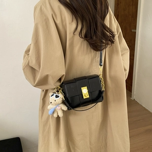 Détail du sac bandoulière en cuir tressé noir avec fermoir doré et ours peluche