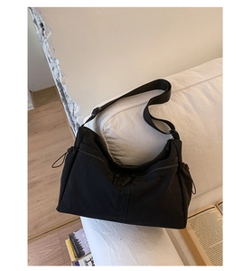 Detail of black large-capacity canvas shoulder bag with wide strap on a white sofa
