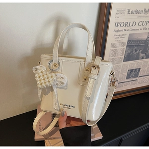 Detail of cream white patent leather bucket bag with pearl heart charm and brand logo