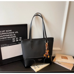 Dettaglio borsa tote in pelle nera con cuciture a contrasto e ciondolo di perline