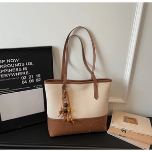 Dettaglio della borsa tote in tela color panna con base in pelle marrone e nappe