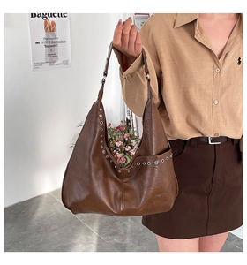 Detail of vintage brown Hobo bag with eyelet studs worn by model in a cozy indoor setting