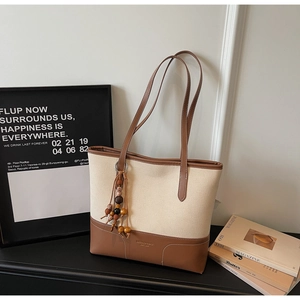 Dettaglio della borsa tote in tela con finiture in pelle marrone e ciondolo decorativo