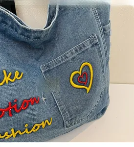 Detail of blue denim tote bag featuring colorful heart embroidery and side pocket texture