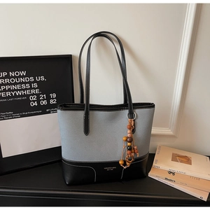 Dettaglio della borsa tote bicolore minimalista con ciondolo di perline in legno stile etnico