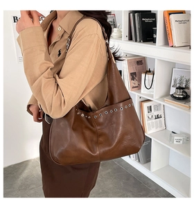 Detail of a brown leather shoulder bag with decorative silver metal eyelets and wide strap
