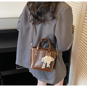Brown leather bucket bag with pearl bow charm worn over a grey blazer and shoulder strap