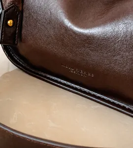 Detail of dark brown lychee grain leather texture with gold rivet and embossed logo