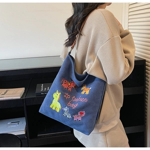 Detail of blue canvas tote bag featuring colorful animal embroidery and leather strap