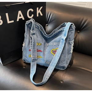 Detail of embroidered 'make fashion' text and heart on blue denim hobo shoulder bag