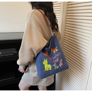 Detail of blue canvas tote bag with cartoon embroidery and leather straps on a model