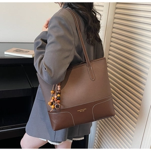 Dettaglio di una borsa tote patchwork bicolore con ciondolo in legno e logo del marchio