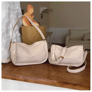 Close-up of beige leather crescent bags in two sizes on a rustic wooden table