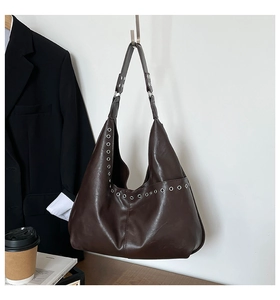 Gros plan d'un sac hobo marron foncé avec œillets métalliques sur mur blanc