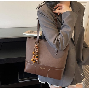 Dettaglio di una borsa tote in pelle marrone scuro con cuciture in tela e nappa di perline