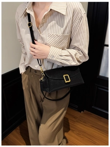 Schwarze quadratische Ledertasche mit Goldschnalle, getragen zu Hemd und Khakihose