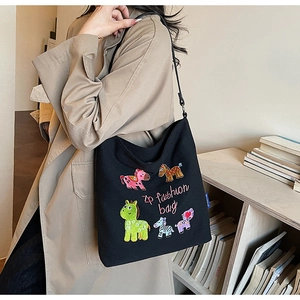 Detail of a black canvas tote with colorful cartoon embroidery on a beige trench coat