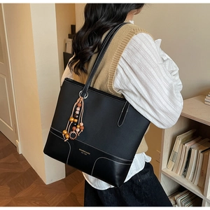 Dettaglio della borsa tote in pelle nera con cuciture a contrasto e un ciondolo con nappa