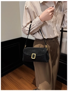 Schwarze Leder-Baguette-Tasche mit goldener Schnalle, getragen von einem Model im Innenraum