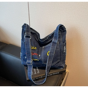 Detailed view of dark blue denim tote bag with vibrant embroidery and frayed edges