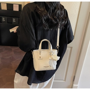 Dettaglio di borsa a secchiello beige con ciondolo a cuore di perle e fiocco in pizzo