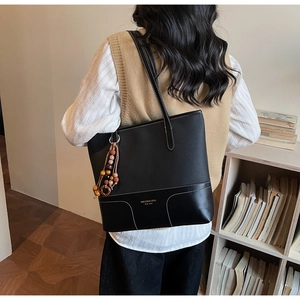 Dettaglio della borsa tote in pelle nera con cuciture a contrasto e ciondolo di perline