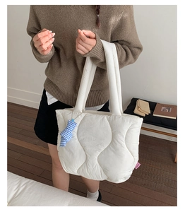 Close-up of white quilted puffer tote bag with blue plaid bow and Fashion woven label