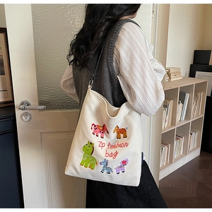 Detail shot of cute cartoon animal embroidery on a cream canvas tote bag with shoulder straps