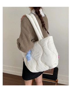 Detail of white quilted tote bag with pink fashion label and blue plaid charm on shoulder strap