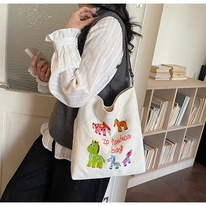Detail of white canvas tote bag with colorful animal embroidery worn by a model