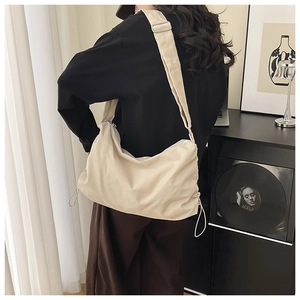 Détail du sac dumpling en nylon beige imperméable porté par un mannequin en intérieur