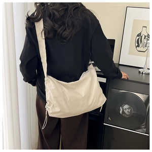 Détail d'un grand sac bandoulière beige en nylon imperméable porté par un modèle