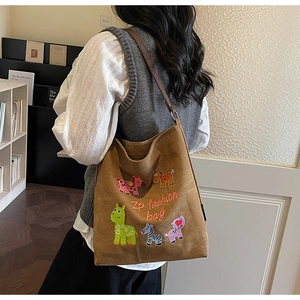 Detail of colorful animal embroidery and leather strap on a brown canvas hobo tote bag