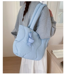 Detail view of light blue quilted puffer tote bag with a checkered bow on a model
