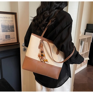 Dettaglio della borsa tote in tela e pelle con nappa e logo del marchio in rilievo
