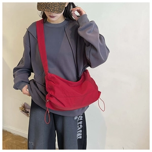 Détail du sac bandoulière en nylon rouge avec cordon de serrage sur un modèle streetwear