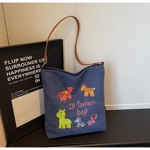 Detail of blue denim tote bag featuring colorful embroidered horses and brown leather strap