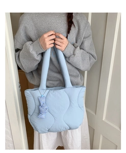 Detail of light blue quilted tote bag with wave stitching and a blue checkered bow charm