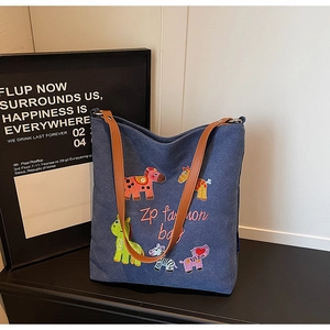 Detail of colorful animal embroidery on blue denim tote bag with brown leather handles