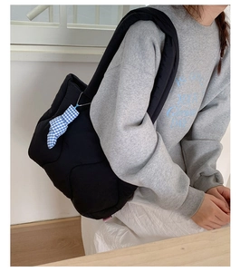 Close-up of black quilted puffer tote bag with ribbon charm and wide shoulder strap