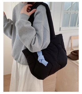 Close-up of a black quilted puffer tote bag with blue and white checkered bow detail
