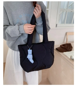 Detail view of a black quilted tote bag with wave stitching and a blue checkered bow charm