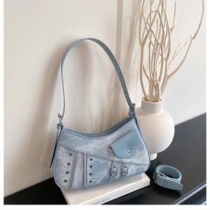 Close-up of light blue denim crescent bag with silver eyelets and metal zippers