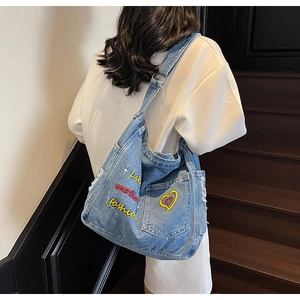 Detail view of denim hobo bag featuring yellow heart and lucky letter embroidery
