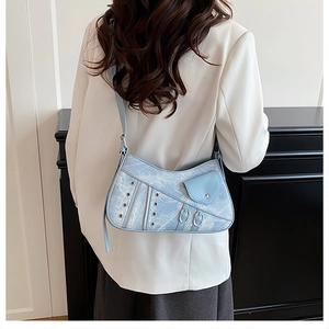 Detail view of denim light blue saddle bag with metallic eyelets and silver buckles